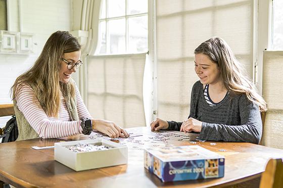 Photo of two Chatham University students working on a jigsaw puzzle at a lounge table